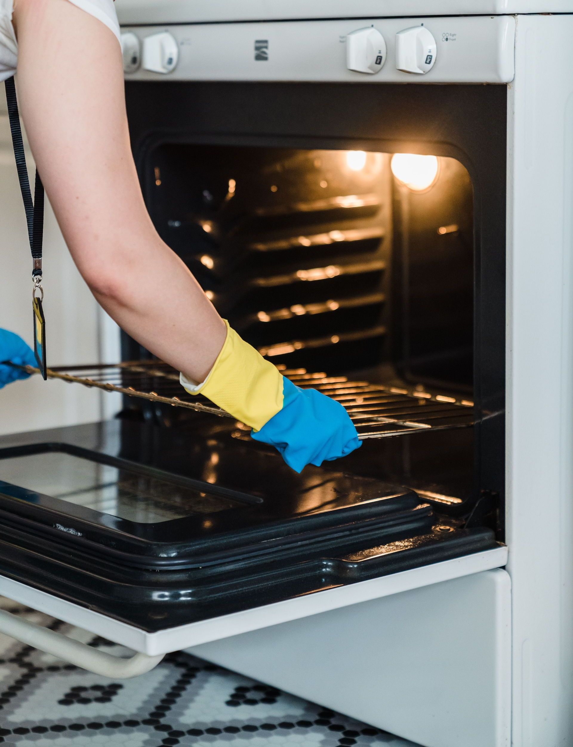 Adult woman cleaning an oven using protective rubber gloves indoors.